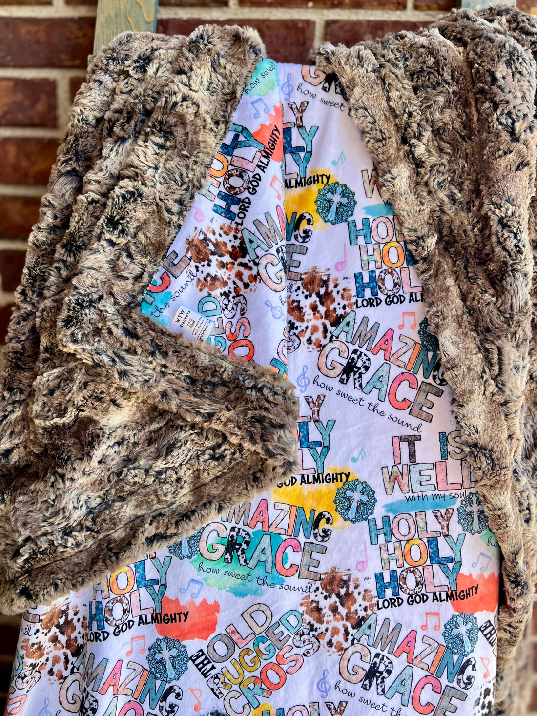 Colorful 'Amazing Grace' fabric with a textured brown fabric overlay against a brick wall.